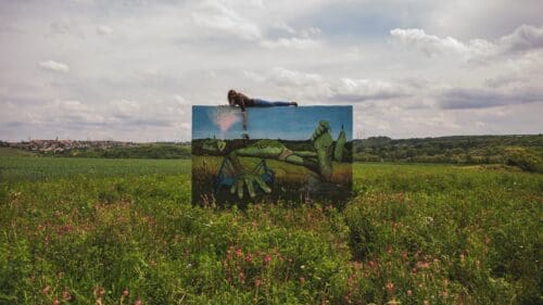 Person liegt auf einem großformatigen, aufgestellten Plane mit einem Kunstdruck im öffentlichen Raum.