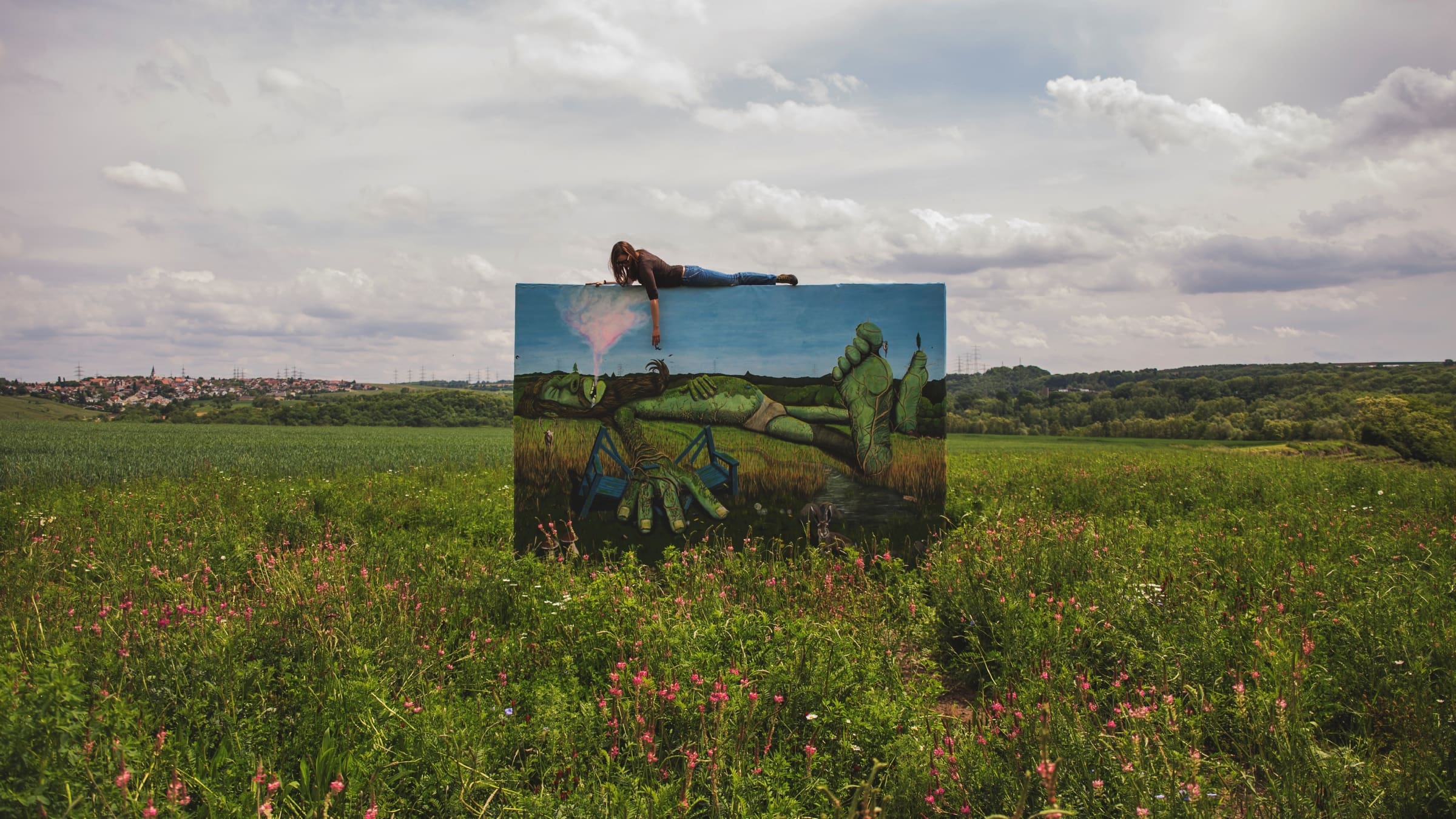 Person liegt auf einem großformatigen, aufgestellten Plane mit einem Kunstdruck im öffentlichen Raum.