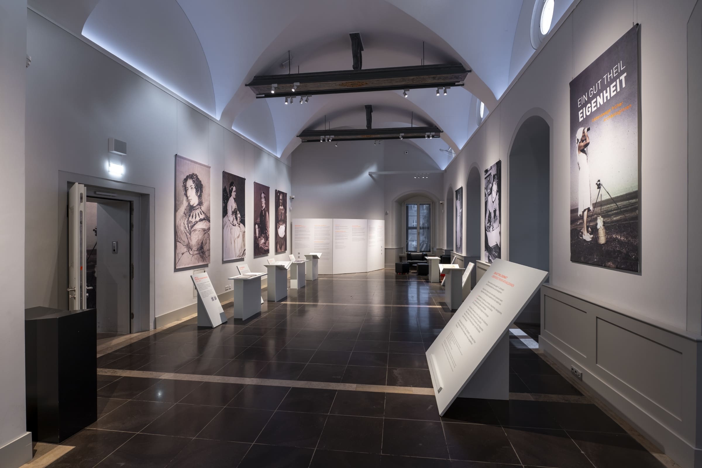 Der Ausstellungsraum mit sieben Wandportraits, Tischen und Texttafeln.