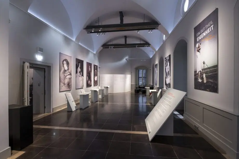 Der Ausstellungsraum mit sieben Wandportraits, Tischen und Texttafeln.