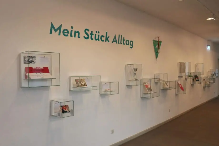 Weiße Wand mit kleinen Vitrinen in unterschiedlicher Höhe, gefüllt mit VfB-Stuttgart-Objekten.