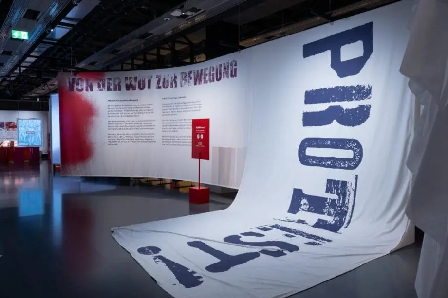 Eingangsbereich der Ausstellung mit einer großen Stoffbahn, auf der "PROTEST" steht.