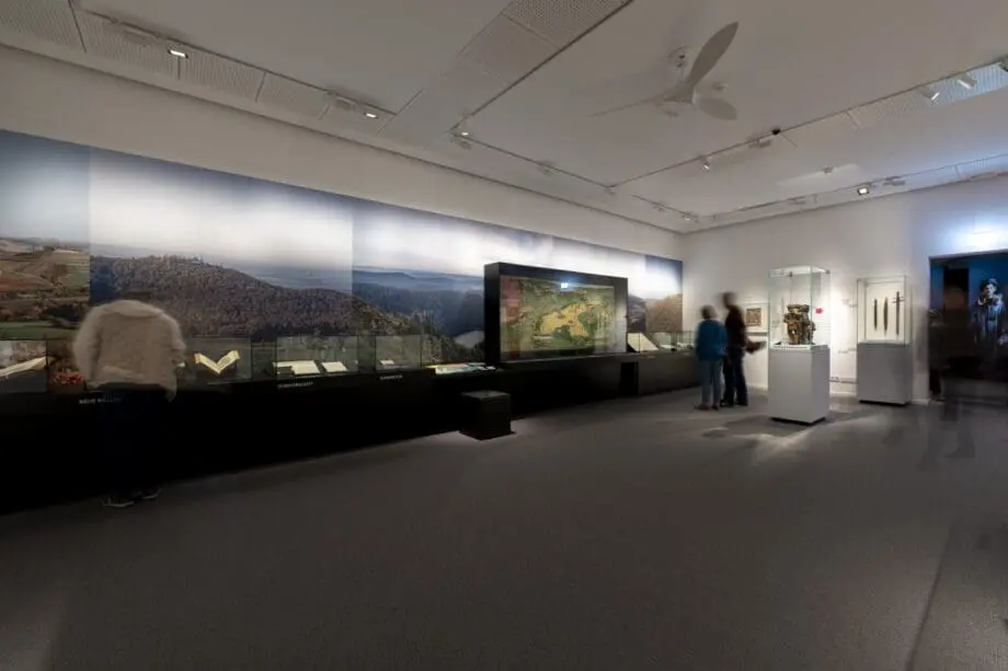 Einblick in Ausstellungsraum, kulturhistorische Objekte, KI-Figuren und inklusive Elemente.