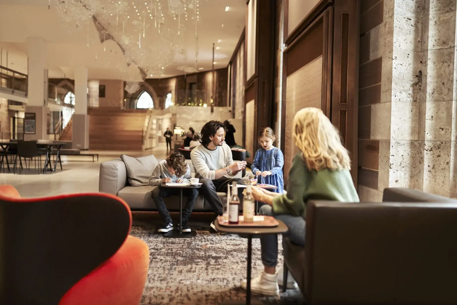 Ein Mann sitzt mit zwei Kindern auf einem Sofa in m Museumsfoyer Dürnitz. Im Vordergrund sotzt eine Frau mit blionden Haaren und grünem Pullover mit dem Rücken zur Betrachterin.