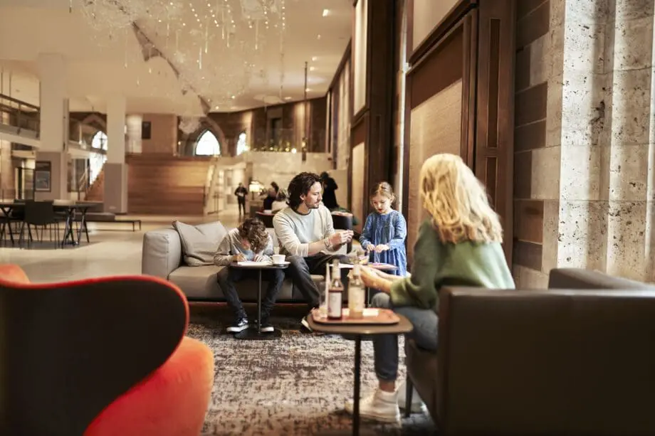 Ein Mann sitzt mit zwei Kindern auf einem Sofa in m Museumsfoyer Dürnitz. Im Vordergrund sotzt eine Frau mit blionden Haaren und grünem Pullover mit dem Rücken zur Betrachterin.